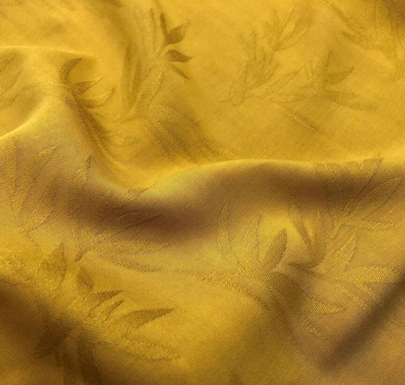 May include: A close-up of a yellow fabric with a subtle embossed leaf pattern. The fabric is soft and has a slightly textured surface.