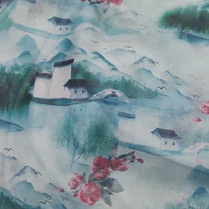 May include: A fabric with a watercolor-style landscape design. The pattern features white buildings, mountains, trees, and red flowers. The color palette includes shades of blue, green, and white, creating a serene and artistic aesthetic.