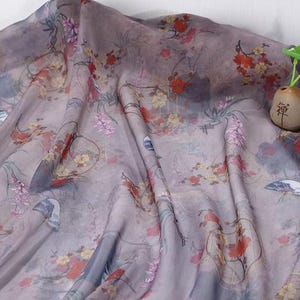 May include: A draped fabric with a floral pattern in shades of lavender, gray, and red. The design includes stylized flowers, fans, and architectural elements. The fabric has a soft, flowing appearance, suitable for apparel or home decor.