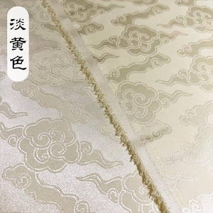 May include: A pale yellow fabric featuring a repeating woven pattern of stylized clouds and swirling wind motifs. The material has a subtle sheen and a frayed edge. A white vertical label on the left side displays the Chinese characters 淡黄色.