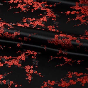 May include: A black fabric featuring a woven pattern of vibrant red cherry blossom branches. The material has a smooth, satin-like sheen, with the floral design appearing in shades of bright red and dark charcoal throughout the textile.