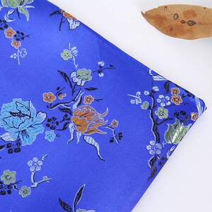 May include: Blue fabric with a floral pattern. The fabric features a repeating design of flowers and leaves in shades of blue, green, orange, and white.