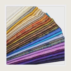 May include: A fan of various fabric swatches in a range of colors, from cream and gold to deep purple and navy. Each fabric displays a paisley pattern. The fabrics are neatly arranged, showcasing the variety of colors and designs.