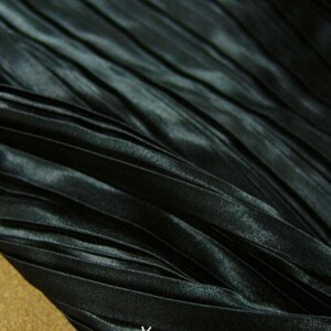 May include: Black pleated fabric with a satin sheen. The fabric is folded and draped, showing the texture of the pleats.