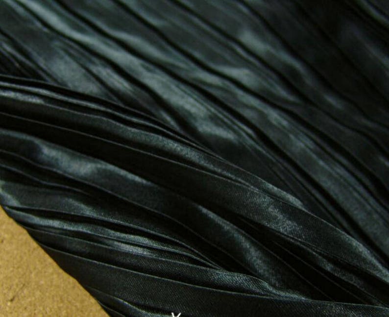 May include: Black pleated fabric with a satin sheen. The fabric is folded and draped, showing the texture of the pleats.