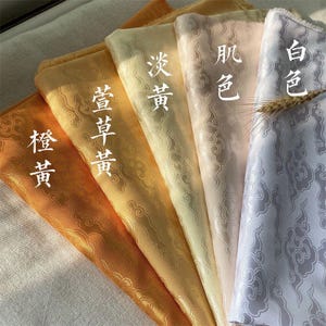 May include: Five folded fabric swatches in a gradient of colours from orange to white, each featuring a tonal cloud pattern. The fabric pieces are labelled with Chinese characters: 橙黄, 萱草黄, 淡黄, 肌色, and 白色, arranged in a row.