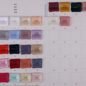 May include: A color swatch chart featuring a variety of fabric samples in a range of colors, including black, white, pink, blue, and brown. Each square sample is approximately 1 inch by 1 inch.