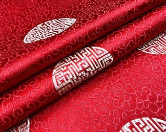 Könnte beinhalten: Roter Stoff mit einem weißen, sich wiederholenden Muster aus chinesischen Doppel-Glückssymbolen. Der Stoff ist in der Mitte gefaltet, sodass das Muster auf beiden Seiten sichtbar ist.
