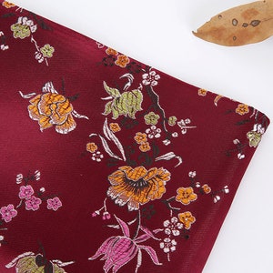 May include: Burgundy fabric with a floral pattern featuring pink, yellow, and green flowers. The fabric has a subtle sheen and a textured surface.