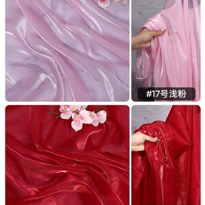 May include: A collection of sheer fabric samples in shades of pink and red. The fabric is draped and folded, showcasing its texture and sheen. The image includes close-ups of the fabric and text in the lower right corner.