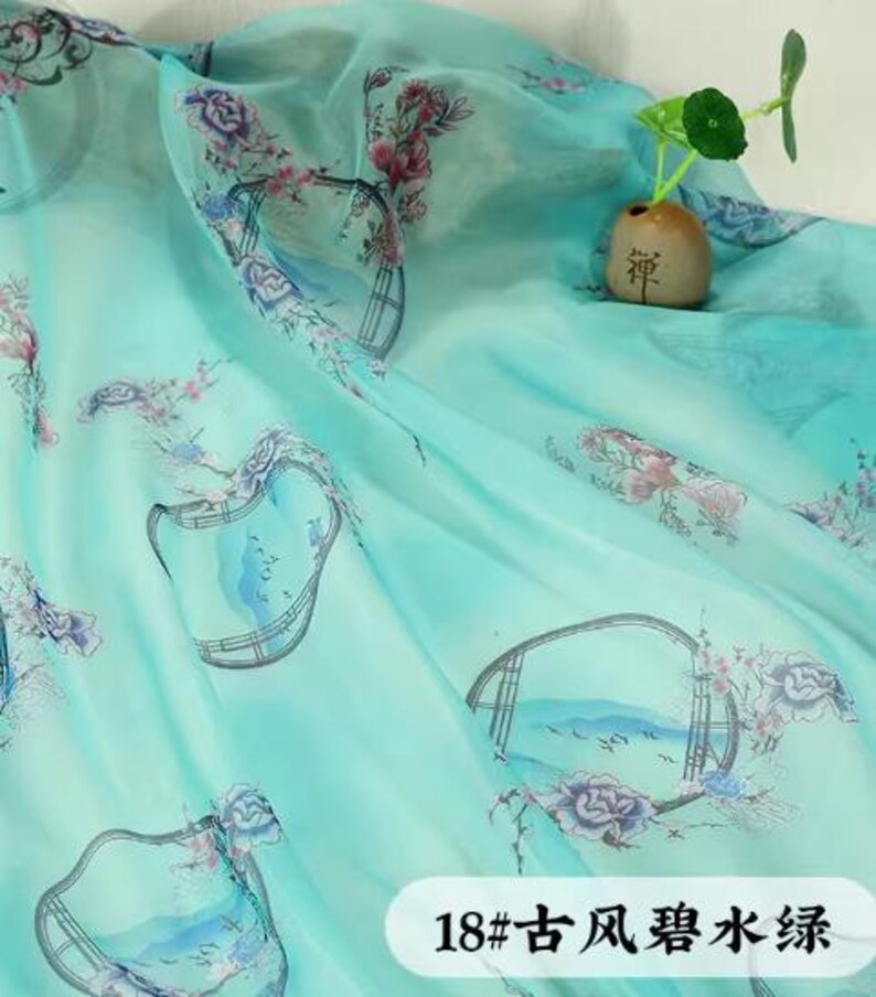 May include: A sheer, turquoise fabric with a floral and landscape print. The fabric has a watercolor effect with pink and purple flowers and a Chinese-style landscape design. The text "18#" and Chinese characters are visible.