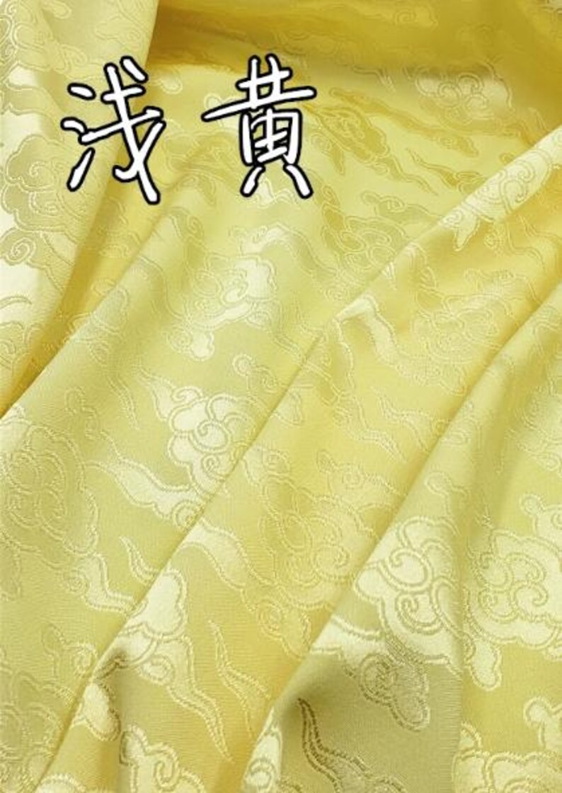 May include: A light yellow fabric featuring a repeating woven pattern of stylized clouds. The material has a subtle sheen and includes the Chinese characters 浅黄 printed in black with a white outline at the top of the textile surface.