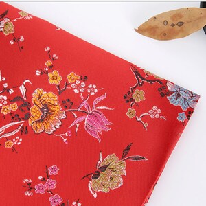May include: Red fabric with a floral pattern. The flowers are in shades of pink, yellow, and blue. The fabric has a subtle sheen.