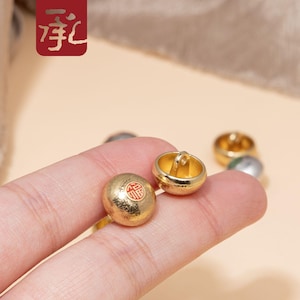 May include: Two gold-coloured buttons with a raised design. One button has a red Chinese character on it. The buttons have a loop on the top for sewing.