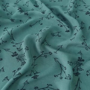 May include: Close-up of teal fabric with a delicate floral pattern. The design features dark gray, stylized sprigs with small flowers, creating a subtle, repeating motif across the textile. The fabric is soft and flowing.