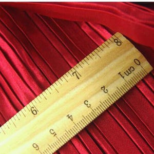 May include: A close-up of a red pleated fabric with a wooden ruler measuring 8 cm. The ruler has black markings for each centimeter.