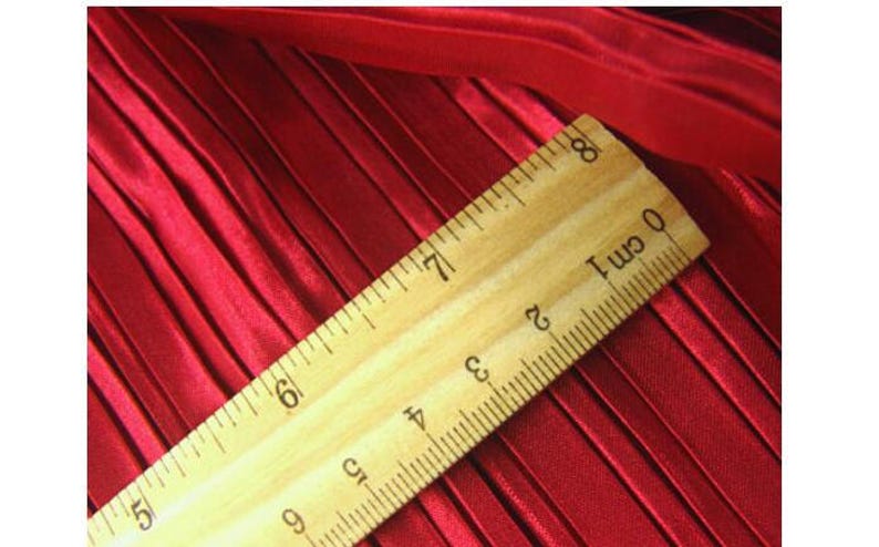 May include: A close-up of a red pleated fabric with a wooden ruler measuring 8 cm. The ruler has black markings for each centimeter.
