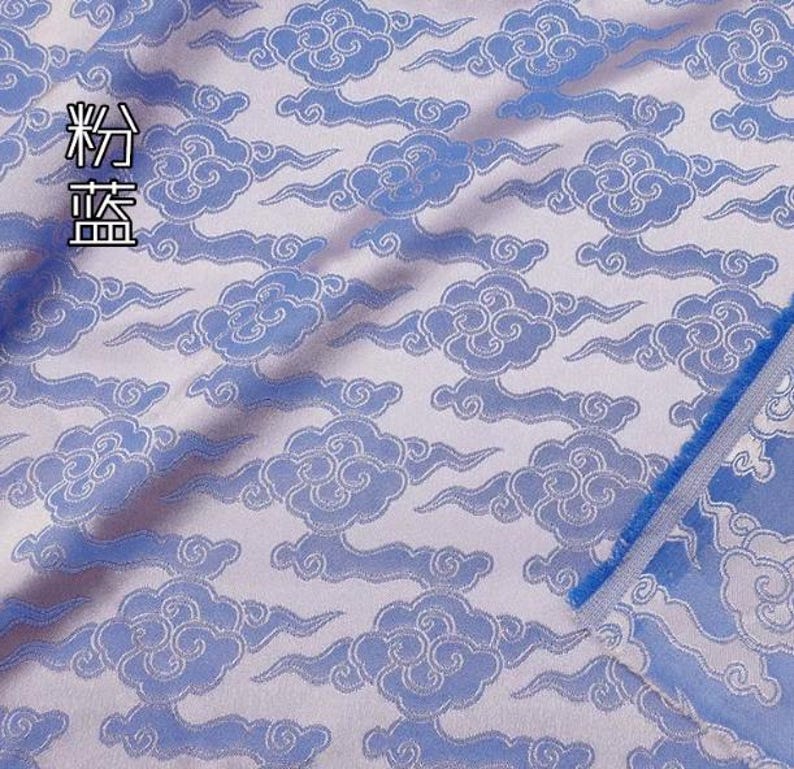 May include: A light blue fabric featuring a repeating pattern of stylized clouds in a darker blue shade. The textile has a woven texture with a visible selvage edge on the right side. The Chinese characters 粉蓝 are printed in the upper left corner.