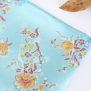May include: A light blue fabric with a floral pattern. The flowers are yellow, orange, red, and white. The fabric has a subtle sheen.