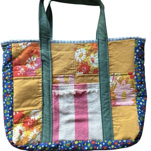 May include: A patchwork tote bag with a variety of fabrics. The bag features a mustard yellow, floral, and striped pattern. The handles are a dark green color, and the edges are trimmed with a blue floral fabric.