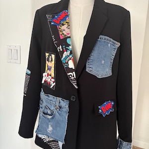 May include: A black blazer featuring a pop art comic book print on the inner lapel, a blue denim pocket on the left chest, a large denim patch pocket on the lower right, and various comic-style patches including the word BANG in red and blue.