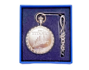 May include: A silver-toned pocket watch featuring an engraved image of the RMS Titanic and the text "RMS TITANIC" on its circular cover. The watch includes a matching silver chain with a clip and is presented in a blue box with a dark blue velvet insert.