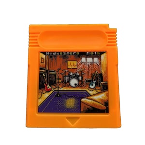 Puede incluir: Un cartucho de videojuego naranja con una etiqueta de arte de píxeles con el texto Midwestern Math. La etiqueta representa una escena de estudio de música con una batería, guitarras, amplificadores y un soporte de micrófono en una habitación.
