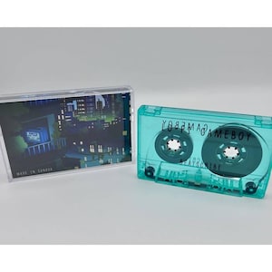 Può includere: Una musicassetta turchese con le parole "GAMEBOY" e "BEATSCRINE" stampate sopra. La custodia della cassetta è trasparente e il nastro all'interno è visibile. È presente anche una seconda custodia per musicassetta con una scena notturna della città.