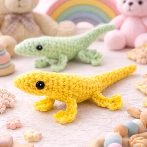 Può includere: Due giocattoli a forma di lucertola all'uncinetto, uno giallo e uno verde, con occhi neri, sono al centro dell'immagine. I giocattoli sono circondati da altri peluche, tra cui un orsacchiotto, un coniglietto e un arcobaleno. Piccole decorazioni in legno e floreali completano la scena.