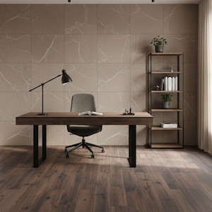 May include: A modern office space featuring a dark wood desk with black legs, a gray office chair, and a black desk lamp. A bookshelf with books and plants stands to the right. The walls are a light brown with white veining.