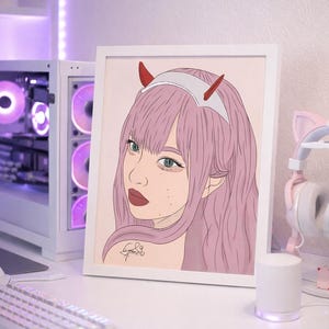 May include: A framed anime-style illustration of a woman with pink hair, red horns, and green eyes. The artwork is set on a white desk with a keyboard, mouse, and a computer tower with purple lighting. A pair of pink cat ear headphones are visible.