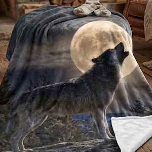 Peut inclure: Une couverture gris foncé représentant un loup hurlant à la pleine lune. La couverture a une texture douce et un dessous blanc. La scène comprend une forêt et un ciel nocturne.