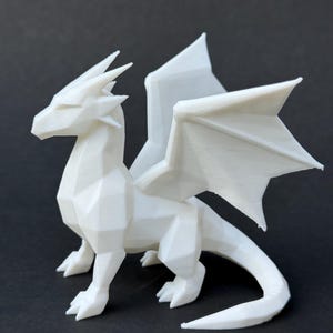 May include: A white, geometric dragon figurine with detailed wings, legs, and a tail. The dragon is posed on a dark surface, showcasing its angular design. The figurine is a fantasy-themed decorative item.