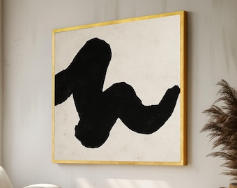May include: Abstract art print featuring a large, black, brushstroke-like shape against a cream-colored background. The artwork is framed in a gold-colored, square frame, adding a touch of elegance to the piece. The overall aesthetic is minimalist and modern.