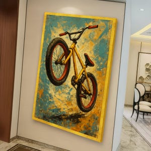May include: A framed canvas art print featuring a yellow BMX bicycle in mid-air against a blue and yellow abstract background. The bicycle has red accents on the tires and handlebars, and a red seat. The frame has a gold border.