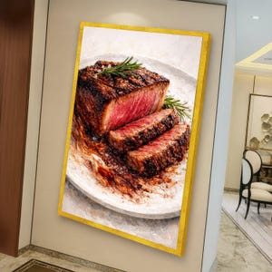May include: A framed canvas art print of a cooked steak, sliced to reveal the pink interior. The steak is on a white plate, garnished with rosemary and salt. The frame is gold.