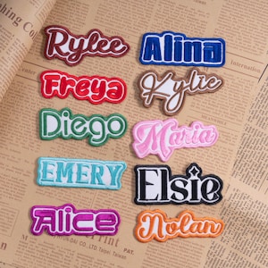 May include: A collection of embroidered name patches in various colors, including red, blue, pink, and green. Each patch features a different name in a stylized font, such as "Rylee," "Alina," and "Freya." The patches are displayed on a vintage newspaper background.