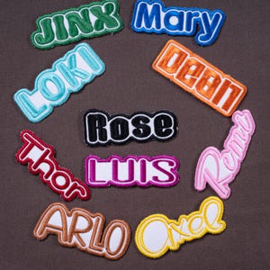 May include: Assortment of embroidered name patches in various colors. Names include "Jinx", "Mary", "Loki", "Dean", "Rose", "Thor", "Luis", "Remy", "Arlo", and "Axel". Each patch features a contrasting border.