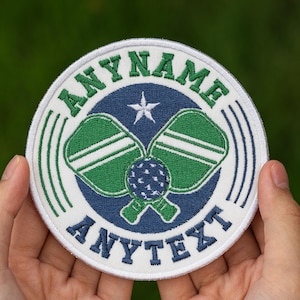 May include: Round embroidered patch featuring a pickleball design. The patch has a white border with the text "ANYNAME" and "ANYTEXT" in green. The center features two green and white pickleball paddles and a blue pickleball ball. A white star is in the center.