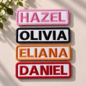 May include: Four rectangular embroidered name patches with white backgrounds and colored borders. The top patch has a pink border and the name HAZEL in pink. The second has a black border and OLIVIA in black. The third has an orange border and ELIANA in orange. The bottom has a red border and DANIEL in red.