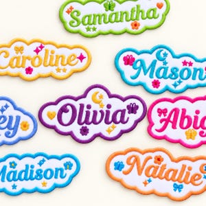 May include: A collection of cloud-shaped embroidered name patches featuring the names Samantha, Caroline, Mason, Olivia, Abigail, Madison, and Natalie. Each patch has a white background with colorful borders and decorative icons like butterflies, stars, and flowers.