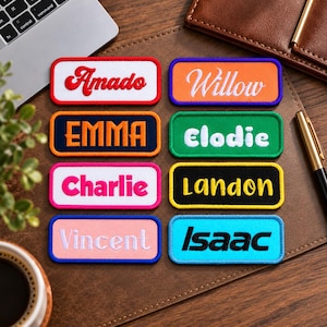 May include: Eight rectangular embroidered name patches with rounded corners. The patches feature the names Amado, Willow, EMMA, Elodie, Charlie, Landon, Vincent, and Isaac in various colors, fonts, and border styles on a brown leather surface.