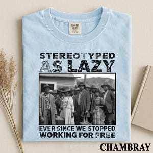Puede incluir: Una camiseta azul claro con el texto negro STEREOTYPED AS LAZY EVER SINCE WE STOPPED WORKING FOR FREE y una fotograf&iacute;a en blanco y negro de un grupo de personas con vestimenta hist&oacute;rica frente a un edificio.