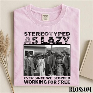 Puede incluir: Una camiseta rosa claro con una fotograf&iacute;a hist&oacute;rica en blanco y negro de un grupo de personas con ropa formal. El texto "STEREOTYPED AS LAZY" aparece sobre la imagen y "EVER SINCE WE STOPPED WORKING FOR FREE" est&aacute; impreso debajo.