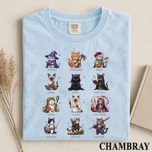 May include: A light blue t-shirt featuring a graphic print of twelve cats dressed as fantasy character classes, including a wizard, barbarian, bard, monk, rogue, warlock, druid, cleric, sorcerer, paladin, ranger, and fighter, with labels below each cat.