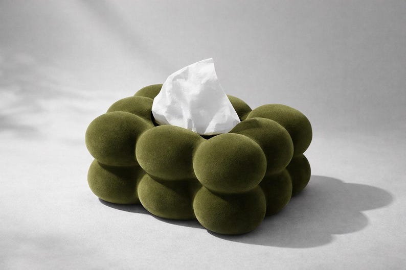 Puede incluir: Cubierta de caja de pa&ntilde;uelos de color verde oliva con un dise&ntilde;o redondeado &uacute;nico. La cubierta tiene un aspecto texturizado y afelpado, con un pa&ntilde;uelo blanco que emerge del centro. El dise&ntilde;o es moderno y adecuado para la decoraci&oacute;n del hogar.
