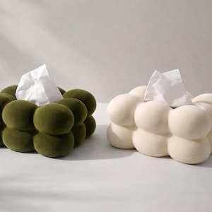 Puede incluir: Dos cajas de pa&ntilde;uelos, una verde oliva y otra blanquecina, cada una con un dise&ntilde;o redondeado en forma de burbujas. Se ven pa&ntilde;uelos blancos saliendo de la parte superior de cada caja. Las cajas est&aacute;n colocadas una al lado de la otra sobre un fondo neutro.