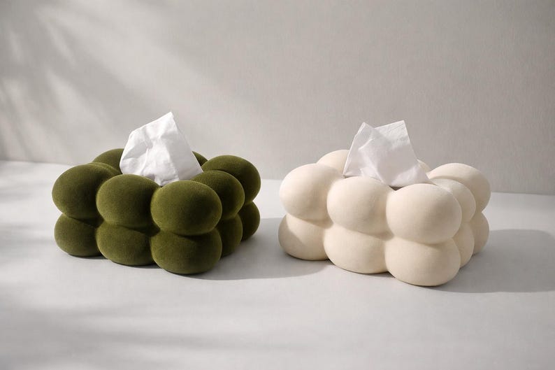 Puede incluir: Dos cajas de pa&ntilde;uelos, una verde oliva y otra blanquecina, cada una con un dise&ntilde;o redondeado en forma de burbujas. Se ven pa&ntilde;uelos blancos saliendo de la parte superior de cada caja. Las cajas est&aacute;n colocadas una al lado de la otra sobre un fondo neutro.