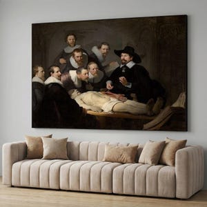 May include: A large framed print of Rembrandt's "The Anatomy Lesson of Dr. Nicolaes Tulp" hangs above a beige sofa. The painting depicts a group of men observing a dissection. The artwork is in a dark, muted color palette.