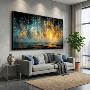 May include: A large framed artwork with a black frame, featuring a solitary figure in a vibrant landscape of blue and gold. The artwork is displayed above a grey sofa with blue cushions, a dark grey throw, and a woven rug.